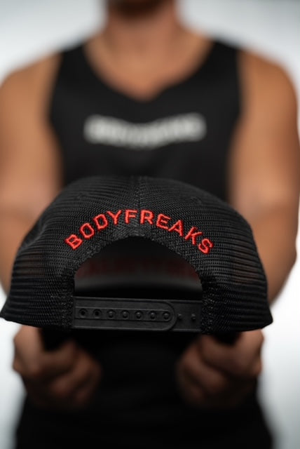 Close-up of a person holding a black cap with "BODYFREAKS" embroidered in red on the back