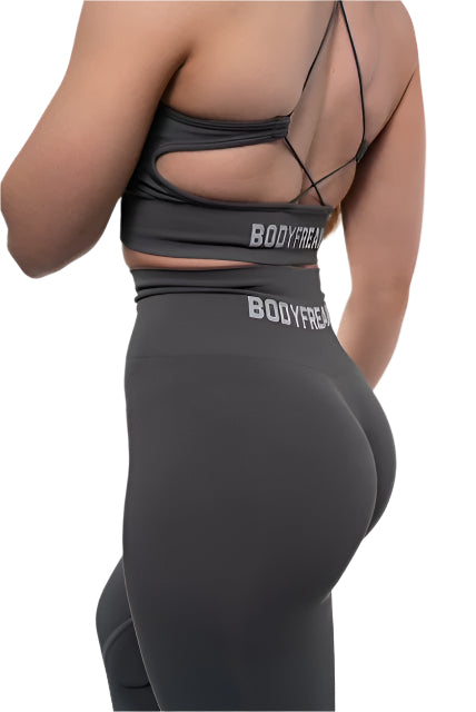 Woman in a Bodyfreaks workout outfit stands next to a black box labeled "BODYFREAKS," facing away
